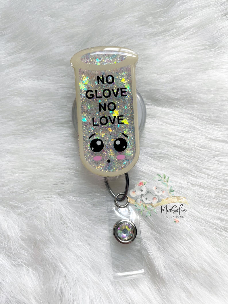 May include: A clear, glitter-filled badge reel with a cute cartoon face and the text "NO GLOVE NO LOVE". The reel is attached to a silver retractable badge holder with a clear plastic badge holder.
