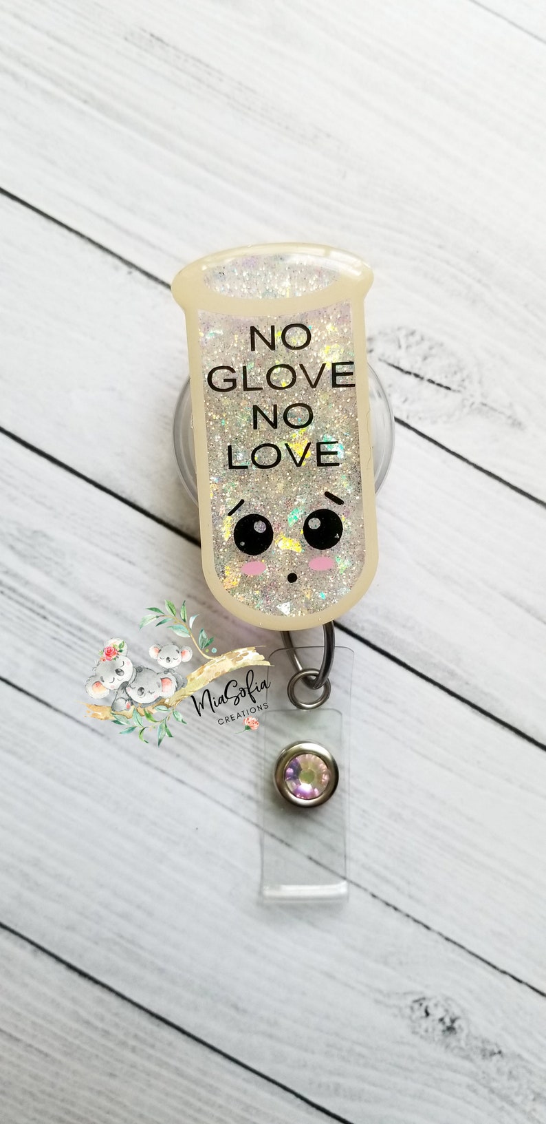 May include: A white glitter badge holder with a cartoon test tube design. The test tube has a face with eyes and blush. The text on the test tube reads "NO GLOVE NO LOVE". The badge holder has a clear plastic strap and a silver swivel clip.