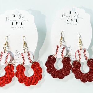 May include: Two pairs of red and white baseball-themed earrings. One pair features a red woven flower-shaped hoop with a white baseball charm. The other pair features a red glitter flower-shaped hoop with a white baseball charm. Both pairs have gold hooks.