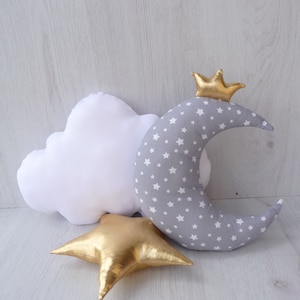 May include: A set of three plush pillows shaped like a cloud, a crescent moon, and a star. The moon pillow is grey with white stars and has a gold crown on top. The cloud pillow is white and the star pillow is gold.