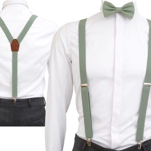 Può includere: Bretelle verde salvia e papillon abbinato sono mostrati su una camicia bianca. Le bretelle hanno clip metalliche color argento e un inserto posteriore in pelle marrone. Il papillon è pre-annodato. L'outfit è adatto per eventi formali.