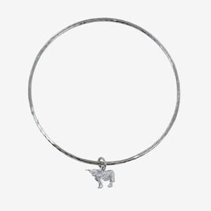 Könnte beinhalten: Ein silbernes Armreif-Armband mit gehämmerter Oberfläche und einem kleinen silbernen Kuh-Anhänger.