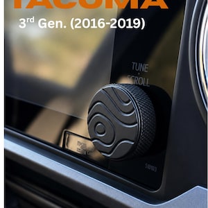 May include: A detailed shot of a car dashboard, highlighting a black control knob with a patterned surface. The image includes the text "TACOMA" in orange and "3rd Gen. (2016-2019)". The knob is for "TUNE" and "SCROLL".