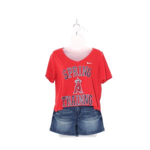 May include: Red v-neck t-shirt with the text "SPRING TRAINING" in blue and white, paired with denim shorts. The shirt has a small Nike logo. The outfit is displayed on a white mannequin.