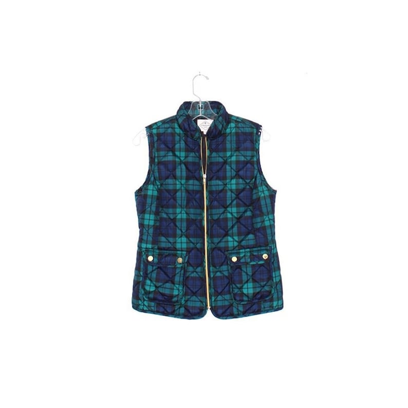 May include: A quilted vest in a plaid pattern of teal and navy blue, with a gold-colored zipper and four gold-colored buttons on the pockets. The vest is hanging on a clear hanger.