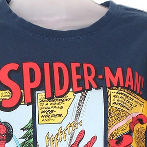 以下が含まれることがあります： ネイビーブルーのTシャツ。コミックパネルのデザインで、赤い文字で「SPIDER-MAN！」と書かれています。デザインには、コミックのテキストとスパイダーマンのイラストが含まれています。