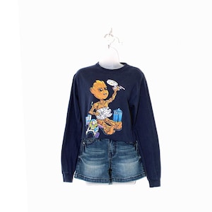 May include: Navy blue long-sleeve shirt with a graphic of Groot from Guardians of the Galaxy, holding a plate and a spaceship, with Buzz Lightyear and a TARDIS. Paired with denim shorts. The shirt is displayed on a white hanger.