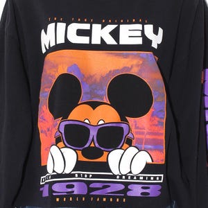 Op de afbeelding: Zwart sweatshirt met lange mouwen met een afbeelding van Mickey Mouse met een paarse zonnebril. Het ontwerp bevat de tekst "THE TRUE ORIGINAL MICKEY", "STOP DREAMING", "1928" en "WORLD FAMOUS". De achtergrond is oranje en paars.