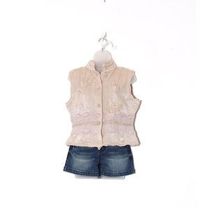May include: A cream-colored, sleeveless vest with floral embroidery and button closures, paired with denim shorts. The vest features a high collar and a delicate lace trim. The shorts are a classic blue wash.