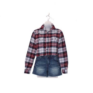 May include: A red, white, and black plaid cropped flannel shirt with two chest pockets, paired with denim jean shorts. The shirt is button-down and has long sleeves. The shorts are a dark wash.