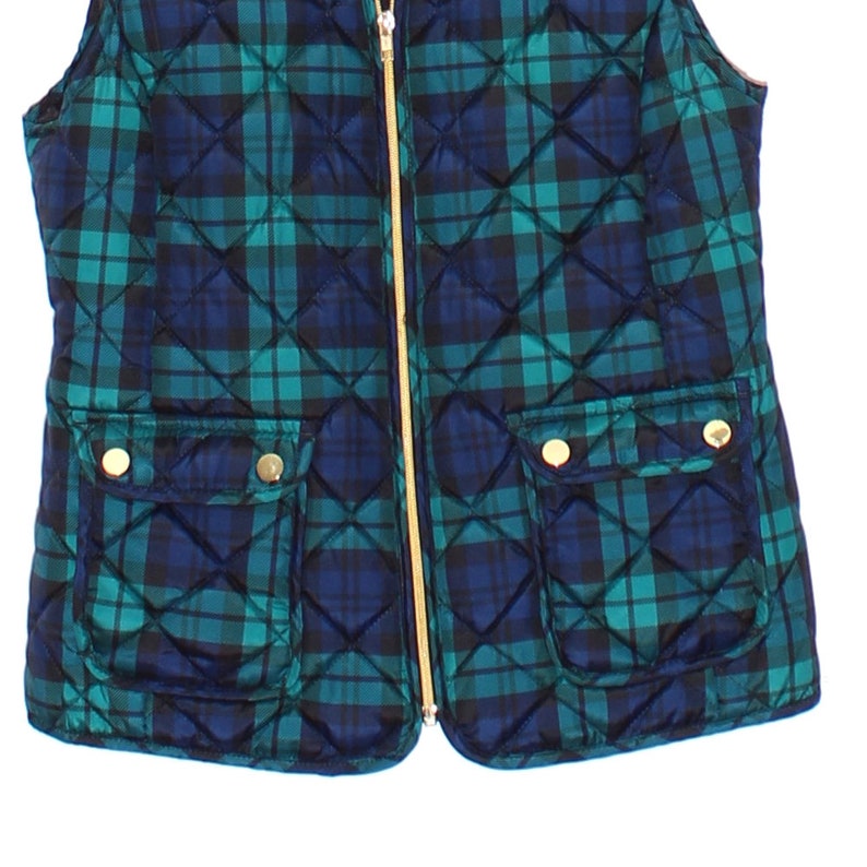 May include: A quilted vest in a plaid pattern of teal and navy blue. The vest has a gold zipper and two front pockets with gold button closures. The vest is a sleeveless garment.