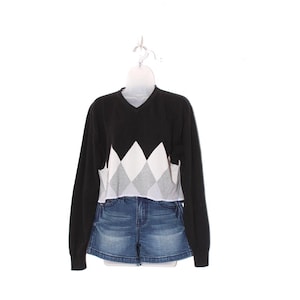 May include: A black long-sleeve sweater with a V-neck and a white, gray, and black diamond pattern on the chest. The sweater is paired with denim shorts. The outfit is displayed on a white mannequin.