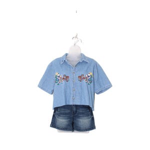 May include: Light blue denim shirt and matching denim shorts. The shirt features embroidered designs of figures and cars. The outfit is displayed on a white hanger against a white background. The shorts are a dark wash denim.