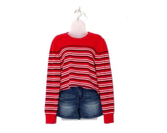 May include: A red long-sleeve shirt with horizontal black and white stripes, paired with denim shorts. The shirt is hanging on a white mannequin and a white hanger against a white background. The shorts are a dark wash.