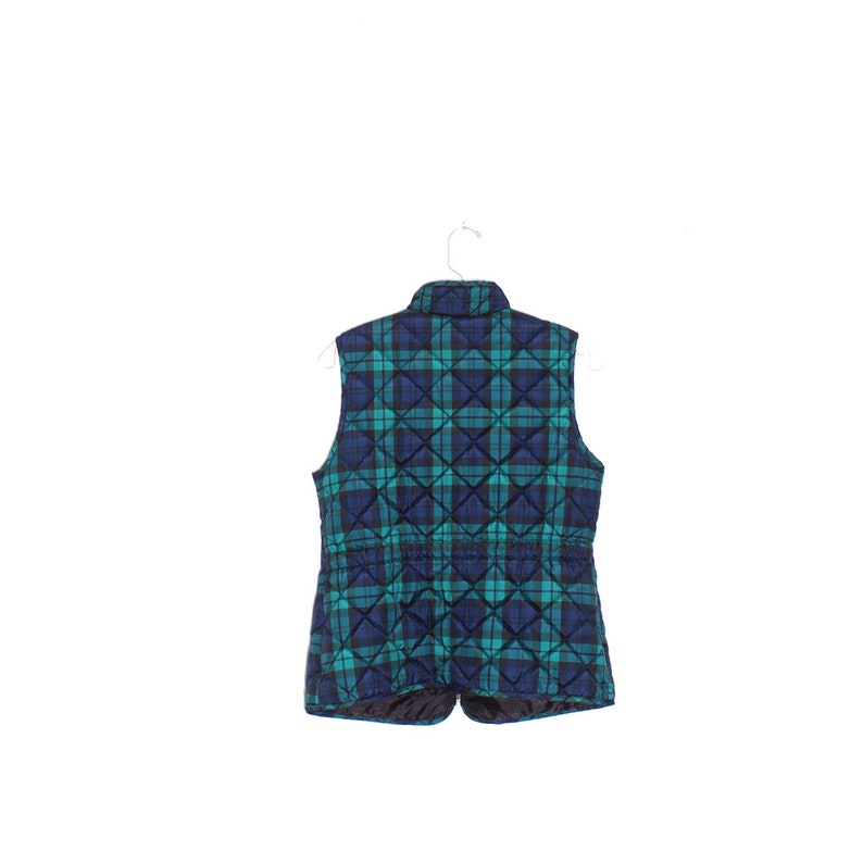 May include: A quilted vest in a plaid pattern of teal and navy blue, hanging on a white hanger. The vest has a stand-up collar and a drawstring waist. The back view shows the full design.