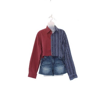 May include: A unique, two-tone shirt with a half-and-half design. One side is a solid burgundy color, and the other is blue with vertical stripes. The shirt is paired with denim shorts, creating a modern, casual look.