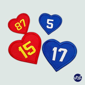 May include: Four heart-shaped patches. Two are red with yellow numbers 87 and 15. The other two are blue with white numbers 5 and 17. The patches have a stitched border.