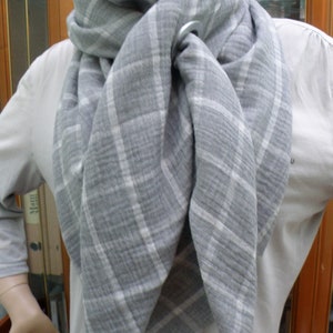 May include: A grey and white checked scarf with a silver ring accent. The scarf is folded and draped around the neck.