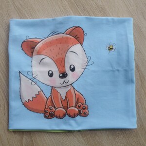 May include: A light blue fabric with a cartoon fox and a bee design. The fox is orange and has a white belly and a fluffy tail. The bee is yellow and black.