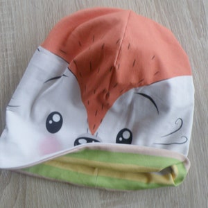 May include: A white and orange beanie with a cartoon fox face and green and yellow stripes on the cuff.