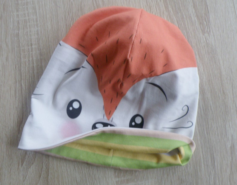 May include: A white and orange beanie with a cartoon fox face and green and yellow stripes on the cuff.
