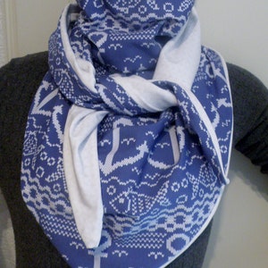 May include: A blue and white patterned scarf with a white border. The scarf is folded and tied around the neck.