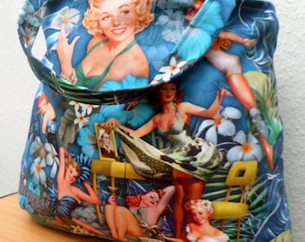 Może przedstawiać: Niebieska torba typu tote z tropikalnym nadrukiem przedstawiającym kobiety w stylu pin-up, liście palmowe i kwiaty. Torba ma dużą kieszeń z przodu i długi pasek.
