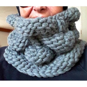 Puede incluir: Una bufanda de cuello de tortuga de punto gris con una textura de punto grueso.