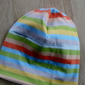 May include: A striped beanie hat with alternating bands of light blue, yellow, green, orange, and beige.