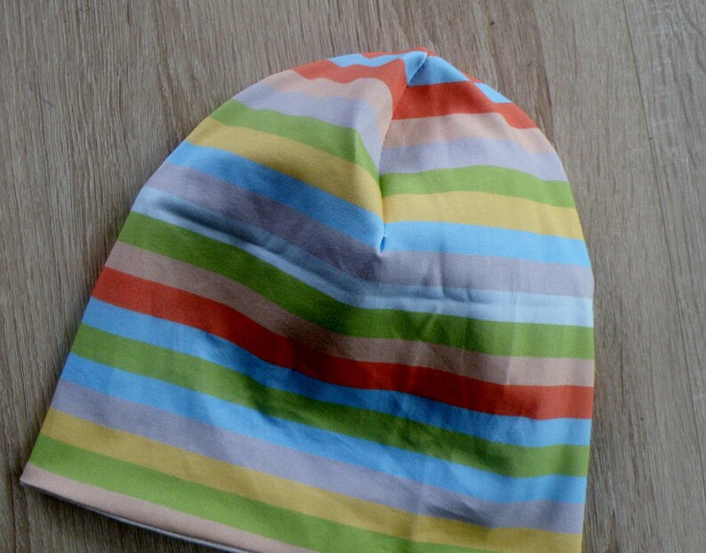 May include: A striped beanie hat with alternating bands of light blue, yellow, green, orange, and beige.