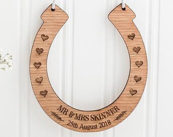 May include: A wooden horseshoe with the text "MR & MRS SKINNER 25th August 2018" engraved on it. The horseshoe is hanging from a white string and has small hearts carved into the wood.