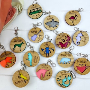May include: A collection of 15 personalised wooden keyrings with various animal and object designs. Each keyring features a different name and a colourful epoxy resin insert. The keyrings are perfect for kids, teachers, or anyone who wants a unique and personalised gift.