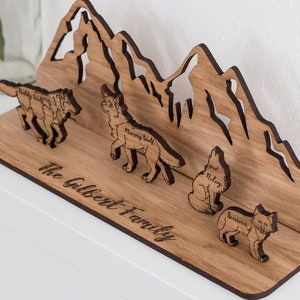 May include: Wooden mountain silhouette with four wolf figures, each with a name engraved on them. The names are "Daddy Wolf", "Mommy Wolf", "Riley", and "Sienna". The base of the mountain is engraved with "The Gilbert Family".