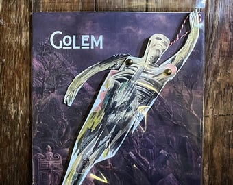 Może przedstawiać: Fioletowa okładka albumu ze słowem "GOLEM" w kolorze białym. Wycięta postać osoby jest przymocowana do okładki za pomocą mosiężnych elementów mocujących. Postać jest stylizowaną ilustracją o szkieletowym wyglądzie, ze złotymi i zielonymi akcentami.