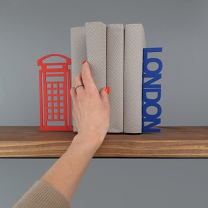 May include: Red and blue metal bookends shaped like a London telephone booth and the word "LONDON". The bookends are holding up three books with gray patterned covers.
