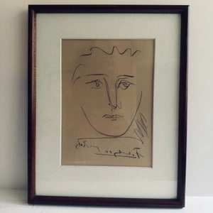May include: A black and white line drawing of a person's face on a beige background. The drawing is signed "Picasso" in the bottom right corner.