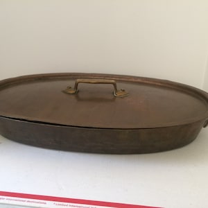 May include: An oval copper roasting pan with a lid and brass handles. The pan is in good condition with some signs of wear.