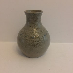 May include: A small, gray ceramic vase with a textured surface and subtle green accents. The vase has a rounded body and a narrow neck.