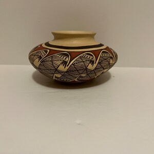 May include: A small, hand-painted pottery vase with a brown and white geometric design. The vase has a rounded body and a slightly flared lip.