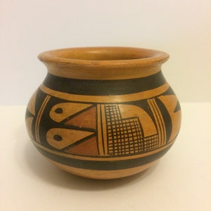 May include: A small, round, brown pottery vase with black and orange geometric designs.