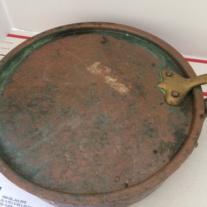 May include: A vintage copper pan with a brass handle. The pan has a green patina and is in good condition.