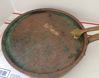 May include: A vintage copper pan with a brass handle. The pan has a green patina and is in good condition.