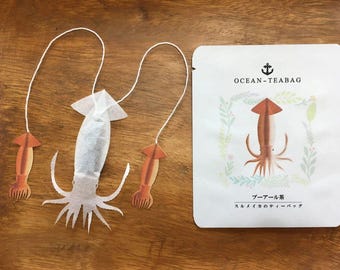 May include: A set of three tea bags shaped like squid. The tea bags are white with brown accents and are packaged in a white envelope with the text "Ocean-Teabag" and "シーフード茶" in Japanese.