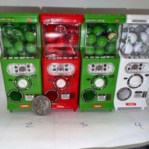 May include: Four miniature gumball machines with clear plastic dispensers. The machines are green, red, and white with the text "Cosmic Code" on the front. The dispensers are filled with green, red, and white gumballs.