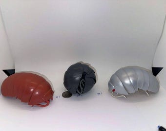 May include: Three large, segmented insect models in a studio setting. One is reddish-brown, another is dark gray, and the third is silver. Each has a rounded, armored appearance, with visible legs and antennae. The models are likely for educational or decorative purposes.