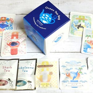 May include: A blue box with the text "Ocean Tea Bag" and an illustration of a teapot with fish inside. The box contains 10 tea bags with different sea creature illustrations and names, such as "Dolphin Tea", "Shark Tea", and "Ocean Beauty".