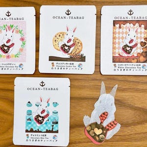 May include: Five white tea bag packets with illustrations of a bunny holding a chocolate heart. Each packet has the text "OCEAN-TEABAG" and Japanese text. One packet has a bunny surrounded by roses, another with a cookie, and another with chocolate.