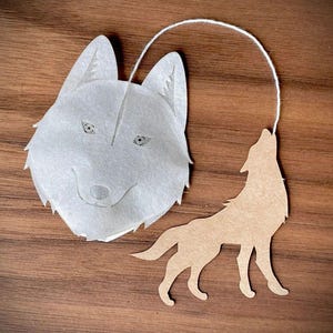 May include: A white wolf tea bag with a brown wolf silhouette hanging from a string. The tea bag is shaped like a wolf's head and has a white background with gray eyes and a black nose.