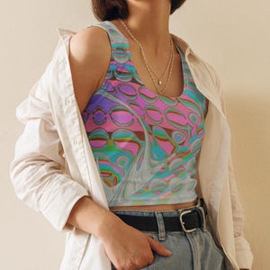May include: A colorful crop top with a swirling pattern in shades of pink, purple, blue, and green. The top is sleeveless and worn with denim shorts, a black belt, and a white button-down shirt.