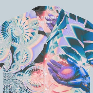 May include: Short-sleeved button-down shirt with a vibrant, abstract design. The shirt features a mix of blue, purple, and peach hues with geometric and floral patterns. The text "AL IN THE MASK BY RACIN" is printed on the collar.